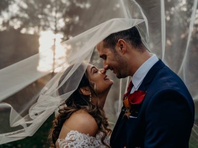 Bride and groom touching noses and smiling under wedding veil